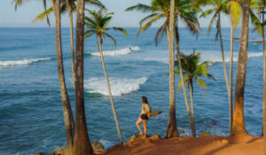 Cheerful woman looking at ocean standing among palm trees grove